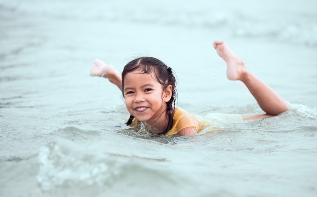 Ragazza asiatica felice del piccolo bambino divertendosi da giocare acqua nel mare nelle vacanze estive