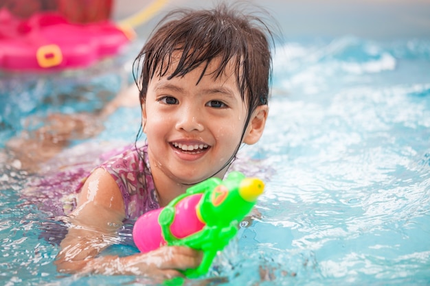 Ragazza asiatica felice del piccolo bambino divertendosi per giocare pistola a acqua e nuoto nello stagno