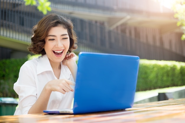 ragazza asiatica felice ridendo e puntando sullo schermo del laptop in ambiente esterno in mattinata