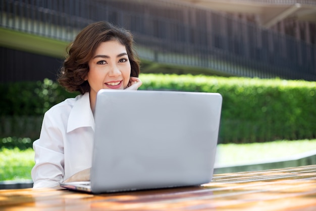 ragazza asiatica felice ridendo e puntando sullo schermo del laptop in ambiente esterno in mattinata