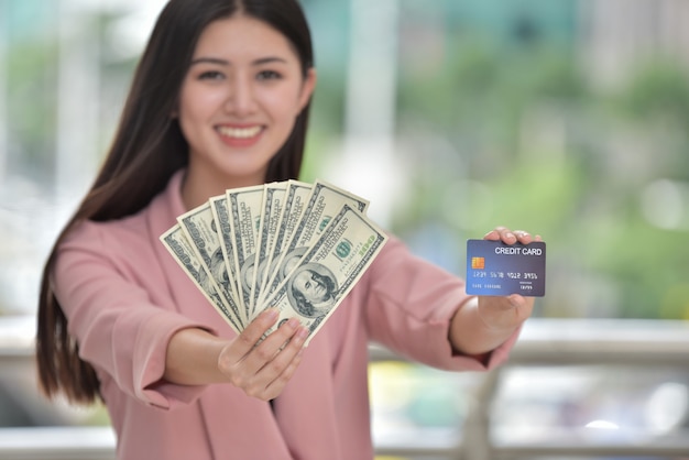 Ragazza asiatica in abito rosa Invia un dolce sorriso a una mano in possesso di una carta di credito.