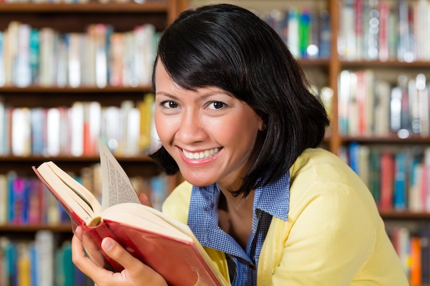 Ragazza asiatica in biblioteca che legge un libro