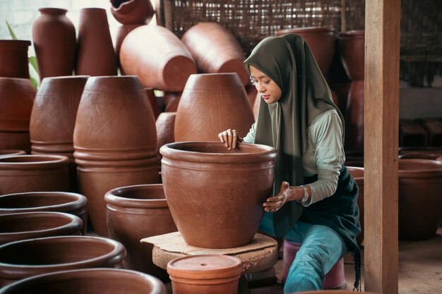 Ragazza asiatica in velo seduto tra pentole per la produzione di ceramiche