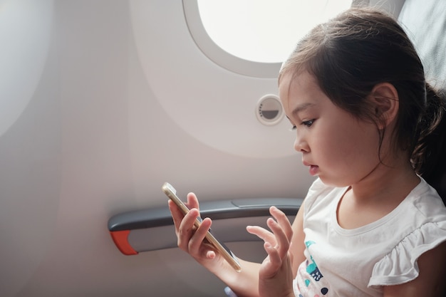 Ragazza asiatica mista utilizzando smart phone in volo, famiglia che viaggia all&#39;estero con i bambini