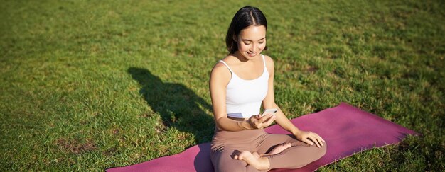 Ragazza asiatica segue l'app di allenamento yoga guardando lo smartphone meditando e facendo esercizi su fresco