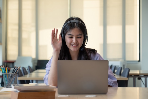 ragazza asiatica sorridente in cuffia che fa una videochiamata sul suo laptop