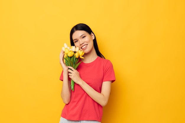 Ragazza asiatica sveglia allegra con un mazzo di fiori sfondo giallo