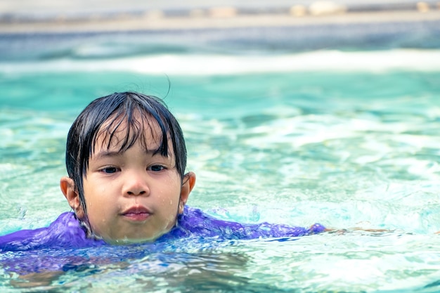 Ragazza asiatica sveglia che galleggia nell'acqua in una piscina