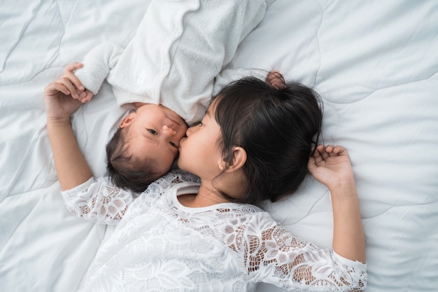 Ragazza asiatica sveglia che pone sul letto con suo fratello del bambino