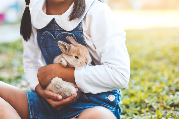 Ragazza asiatica sveglia del bambino che gioca con il piccolo coniglio di coniglietto con amore e tenerezza