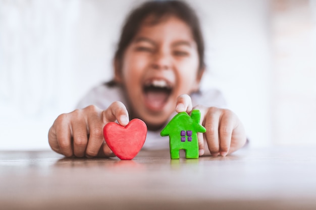 Ragazza asiatica sveglia del bambino che gioca con la casa e il cuore dell'argilla del plasticine con divertimento.