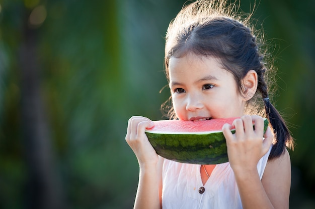 Ragazza asiatica sveglia del piccolo bambino che mangia frutta fresca dell&#39;anguria