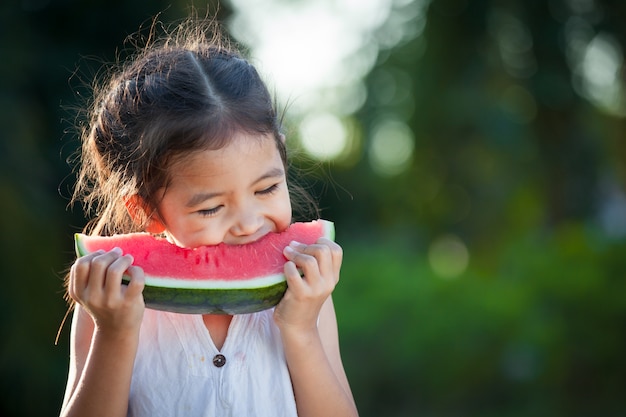 Ragazza asiatica sveglia del piccolo bambino che mangia frutta fresca dell&#39;anguria