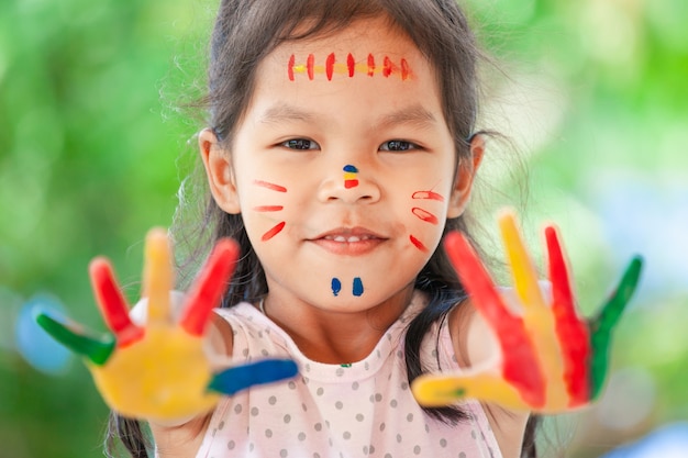 Ragazza asiatica sveglia del piccolo bambino con le mani dipinte che sorride con il divertimento e la felicità