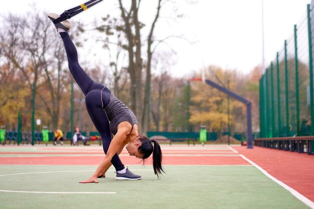 Ragazza atleta formazione utilizzando trx su sportground