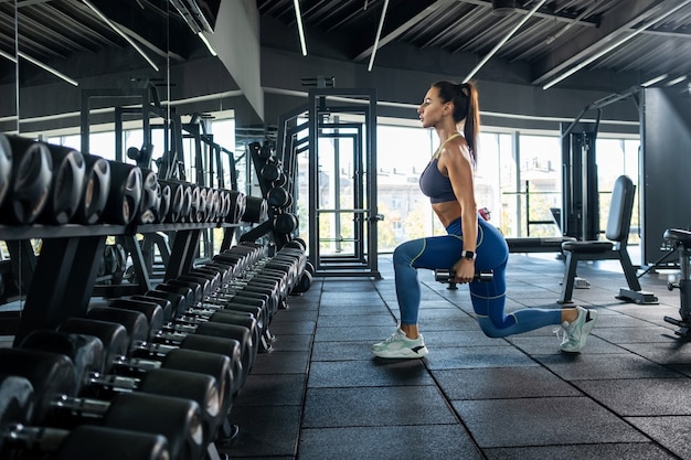 Ragazza atletica che esegue affondo con manubri in palestra