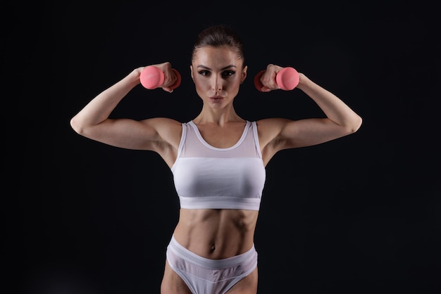 ragazza atletica in vestiti bianchi con manubri che fanno fitness sportivo su uno sfondo scuro