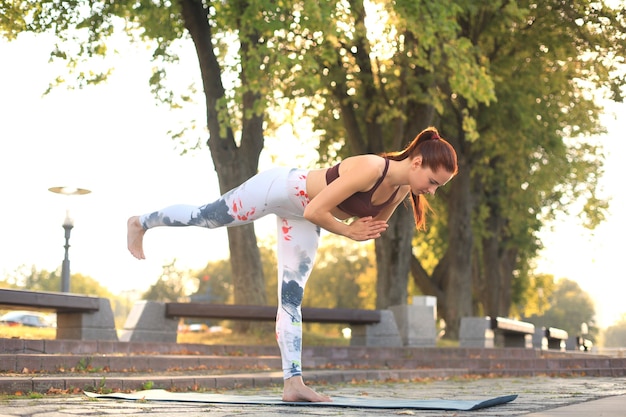 Ragazza atletica sta facendo asana yoga avanzato sul tappetino fitness all'aperto.