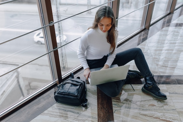 Ragazza attraente che lavora con il computer portatile e le cose in terminale di aeroporto o ufficio sul pavimento. atmosfera di viaggio o atmosfera di lavoro alternativa.