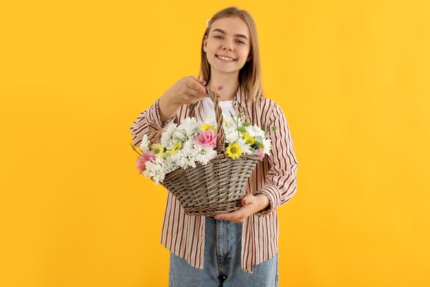 Ragazza attraente con cesto di fiori su sfondo giallo