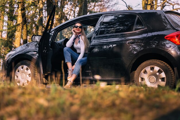 Ragazza attraente con gli occhiali seduta in un'auto nera aperta black