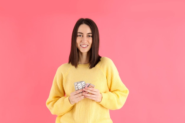 Ragazza attraente con pillole su sfondo rosa