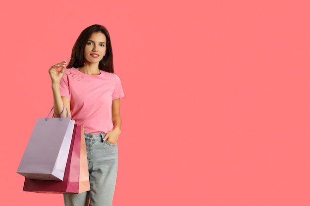 Ragazza attraente con sacchetti di carta multicolori su sfondo rosa.