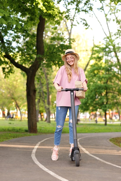 Ragazza attraente con un cappello su uno scooter elettronico nel parco in estate the