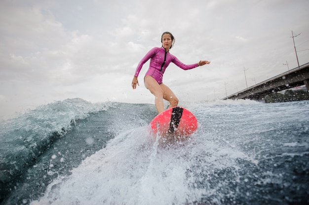 Ragazza attraente dell'adolescente in costume da bagno rosa che guida sul wakeboard arancio