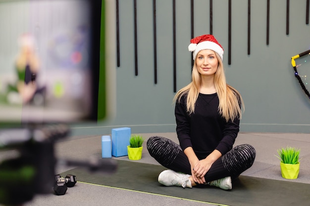 Ragazza attraente in cappello della Santa sta facendo esercizi di fitness e si registra sulla fotocamera.