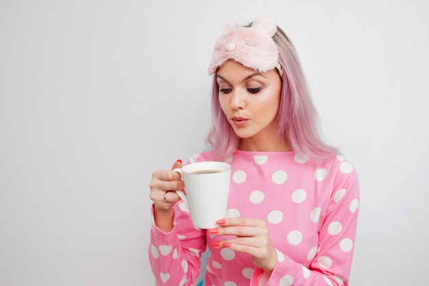 Ragazza attraente in pigiama rosa e maschera per dormire godendo il suo caffè mattutino