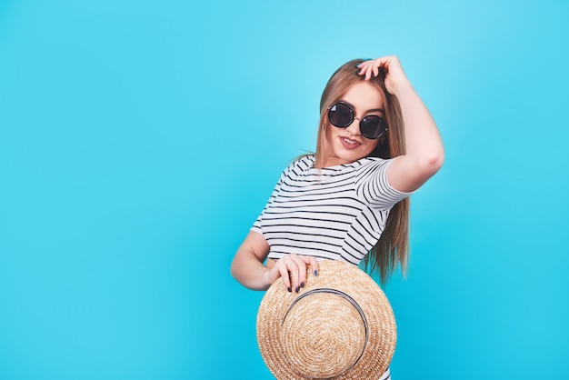 Ragazza attraente in strisce bianche e nere, cappello, occhiali da sole, bocca emotivamente aperta su un blu brillante