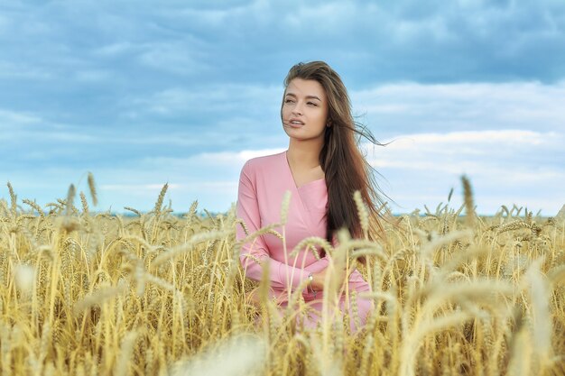 Ragazza attraente in un campo di grano contro il cielo serale