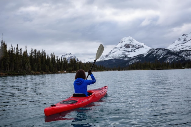 Ragazza avventurosa in kayak in un lago glaciale circondato dalle Montagne Rocciose canadesi