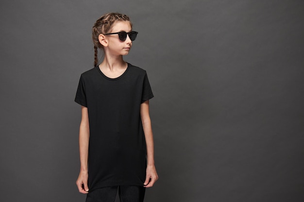 Ragazza bambino che indossa una t-shirt nera con spazio per il tuo logo o design in studio su sfondo grigio con occhiali da sole