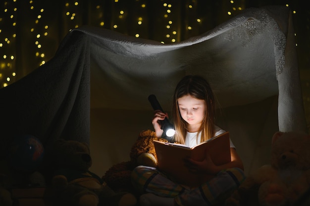 ragazza bambino felice che ride e legge un libro al buio in una tenda a casa