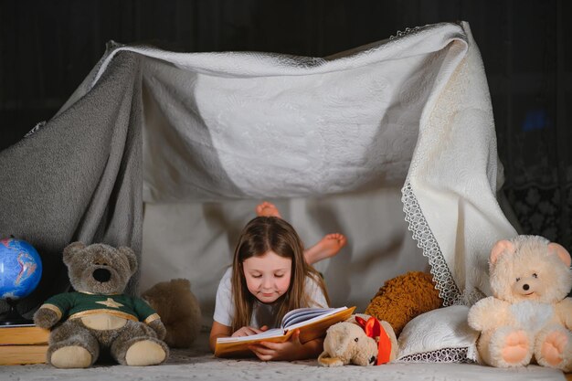 ragazza bambino felice che ride e legge un libro al buio in una tenda a casa