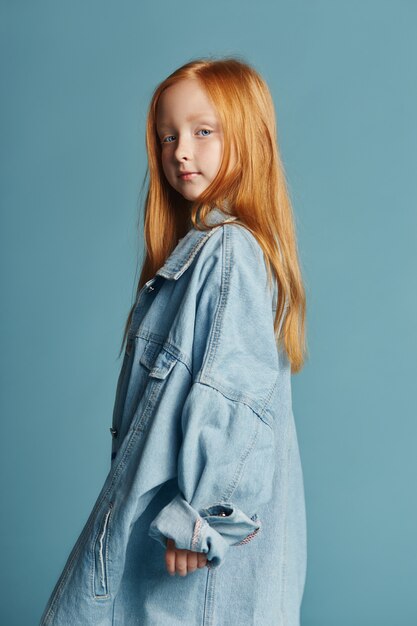 Ragazza bella rossa con i capelli lunghi in una grande giacca di jeans lunga blu