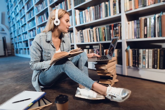 Ragazza bianca che si siede vicino allo scaffale per libri in biblioteca alla notte.