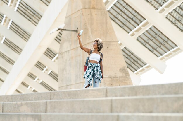Ragazza bionda afro, zaino in città, scatta selfie, viaggiatrice