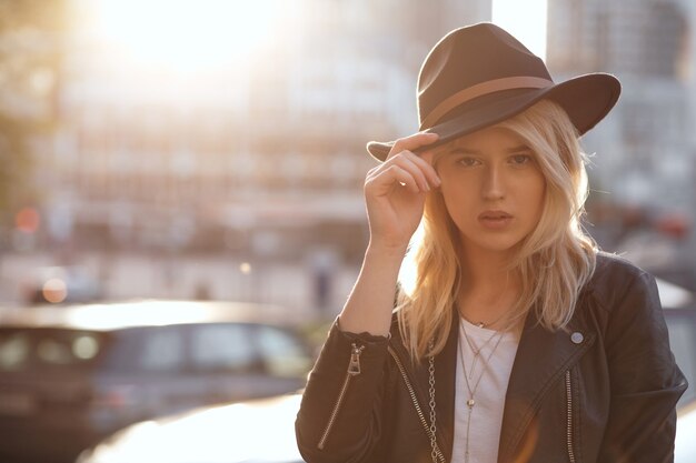 Ragazza bionda alla moda che indossa cappello nero in posa con la calda luce del sole. Spazio per il testo