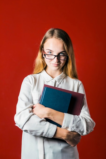 Ragazza bionda attraente felice studente sorridente in camicia bianca con libri su sfondo rosso concetto di studente