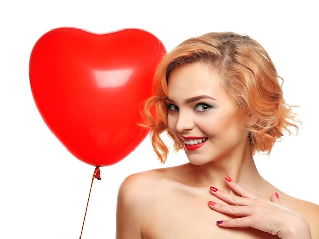 Ragazza bionda attraente giocosa che tiene il pallone rosso del cuore isolato su bianco
