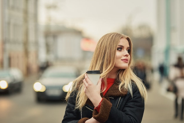 ragazza bionda cammina per la città e beve il caffè