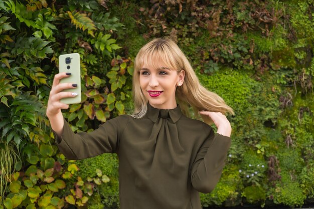 Ragazza bionda caucasica imprenditrice in un parco commerciale in un angolo della natura, che fa una videochiamata, un posto di lavoro moderno