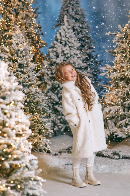 Ragazza bionda caucasica in pelliccia ecologica bianca che cammina nella foresta di natale invernale con luci