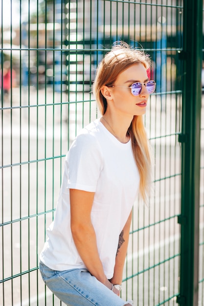 Ragazza bionda che indossa t-shirt e occhiali in posa contro la strada