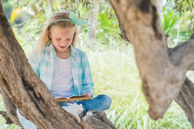 Ragazza bionda che legge un libro su un grande albero di diffusione.