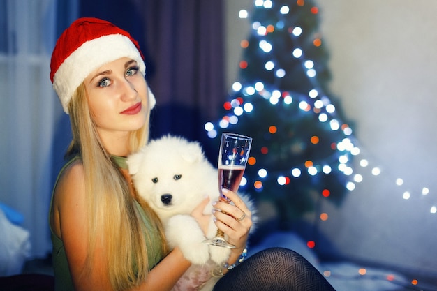 Ragazza bionda con cappello di natale rosso con cane husky samoiedo in decorazioni natalizie