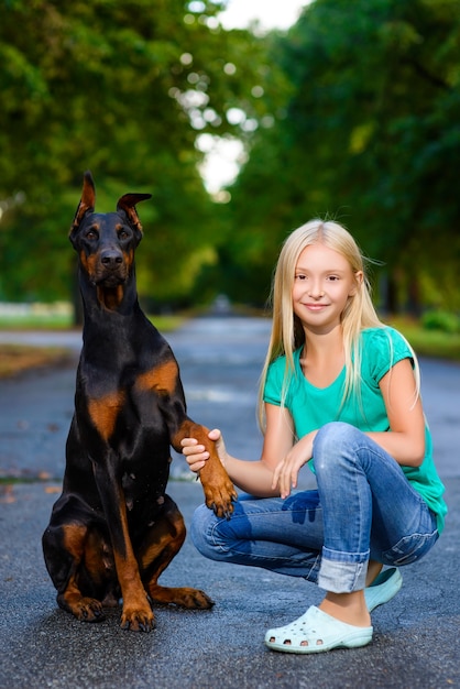 Ragazza bionda con dobermann nel parco estivo.